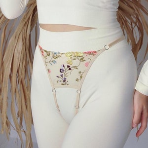May include: Beige lingerie with floral embroidery and adjustable straps. The lingerie has a delicate floral pattern and is made of a soft, sheer fabric.
