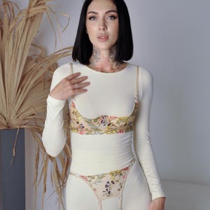 May include: A white long-sleeved top with a floral lace bra and matching floral lace panty. The bra and panty have a delicate floral pattern in shades of pink, yellow, and green.