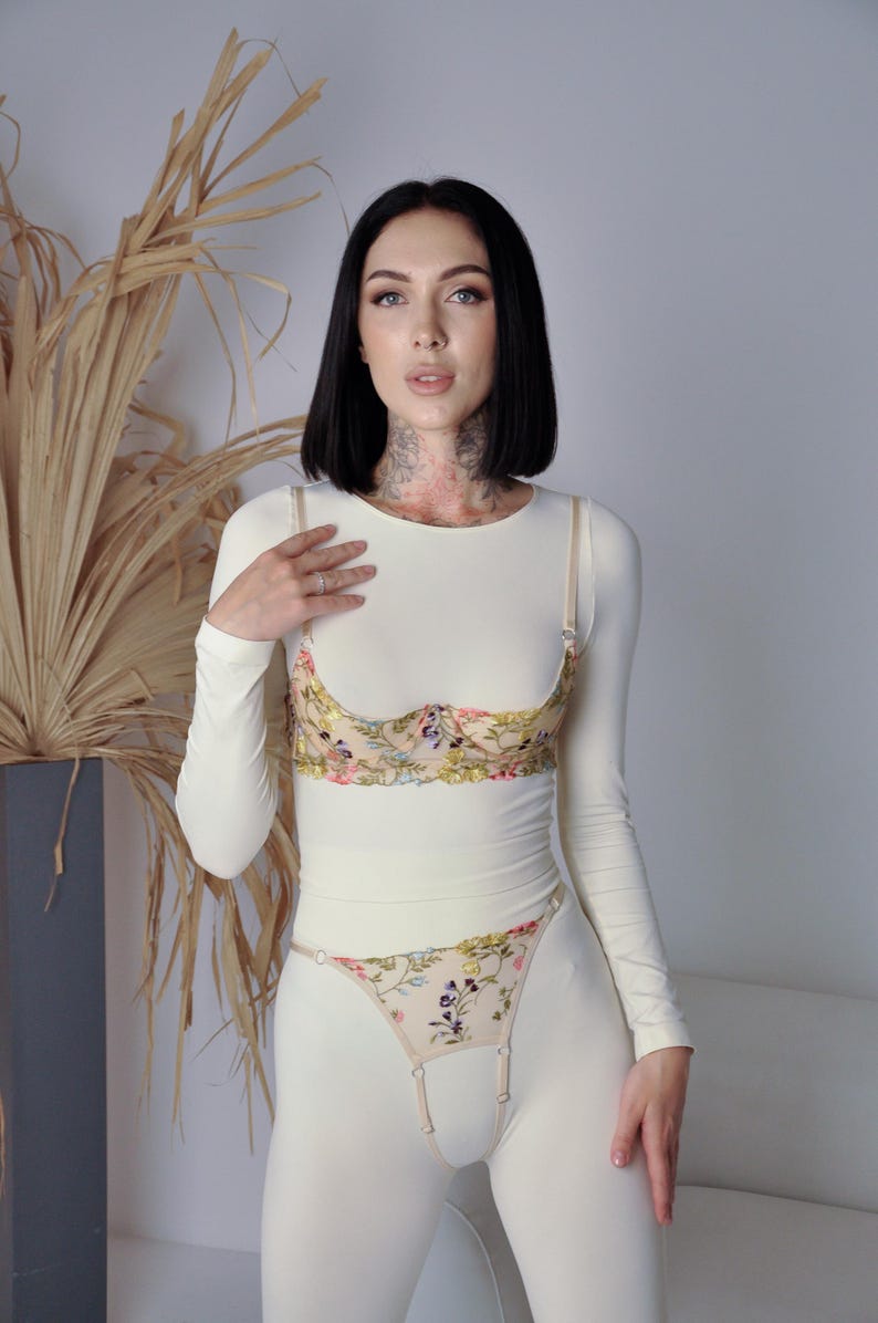 May include: A white long-sleeved top with a floral lace bra and matching floral lace panty. The bra and panty have a delicate floral pattern in shades of pink, yellow, and green.