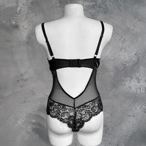May include: Black lace bodysuit with a sheer mesh panel in the back. The bodysuit has a low-cut neckline and adjustable straps.