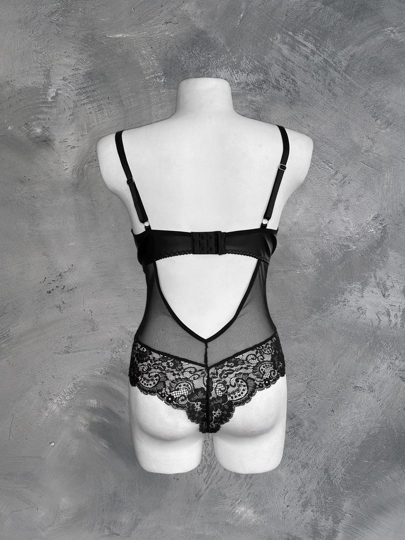 May include: Black lace bodysuit with a sheer mesh panel in the back. The bodysuit has a low-cut neckline and adjustable straps.