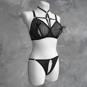 May include: Black lingerie set with a polka dot pattern and a criss-cross strap design. The bra has a halter neck strap and the panty has a cutout detail.