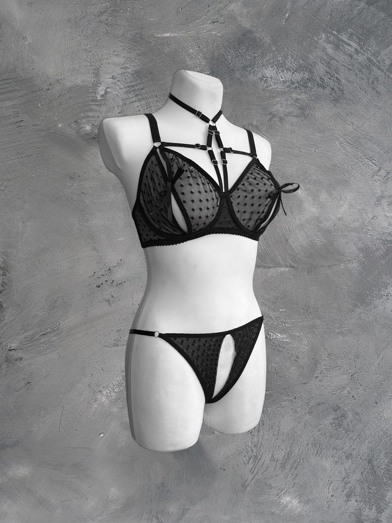 May include: Black lingerie set with a polka dot pattern and a criss-cross strap design. The bra has a halter neck strap and the panty has a cutout detail.