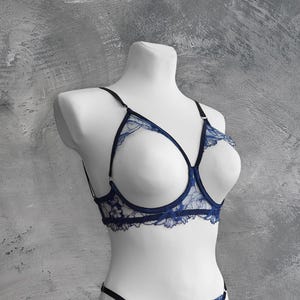 Könnte beinhalten: Ein blauer Spitzen-BH mit zartem Blumenmuster. Der BH hat einen tiefen Ausschnitt und verstellbare Träger.