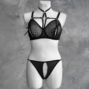 May include: Black lingerie set with a polka dot pattern. The bra has a harness style strap and the panty has a cutout detail.