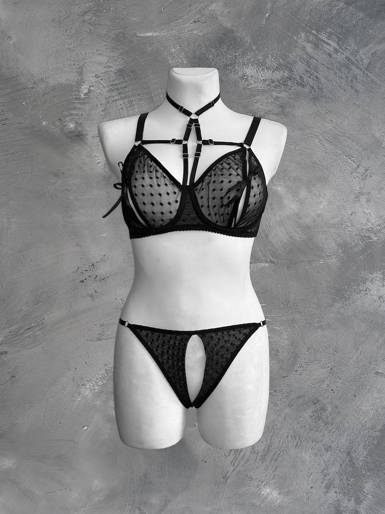 May include: Black lingerie set with a polka dot pattern. The bra has a harness style strap and the panty has a cutout detail.