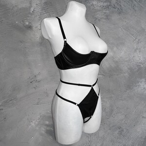 May include: Black lingerie set with a satin bra and a high-cut panty with criss-cross straps.