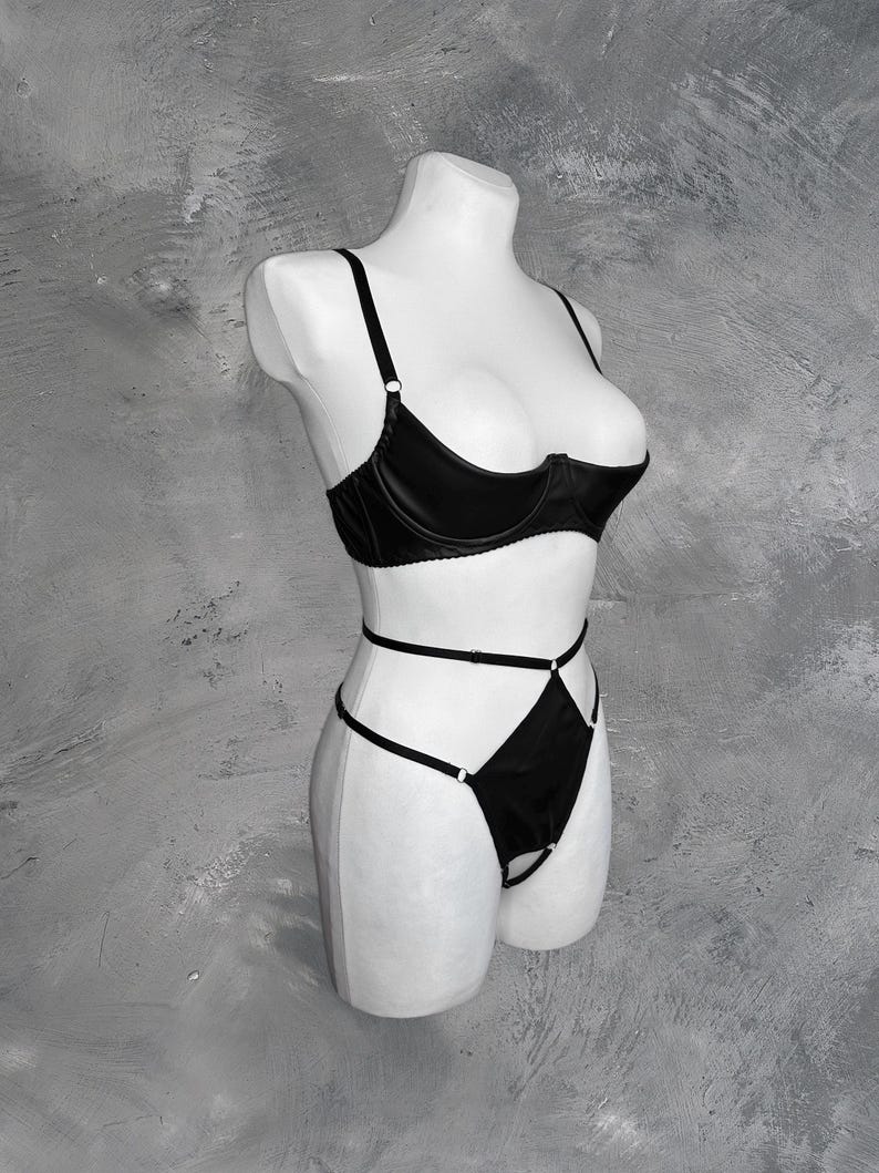 May include: Black lingerie set with a satin bra and a high-cut panty with criss-cross straps.