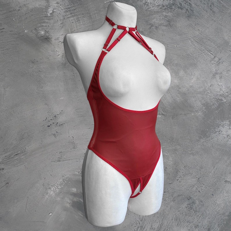 May include: Red mesh bodysuit with a halter neckline and adjustable straps. The straps have silver rings and buckles. The bodysuit has a cutout at the crotch.