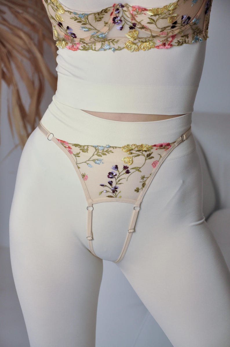 May include: White lingerie set featuring floral embroidery. The top is a cropped tank top with a delicate lace trim. The bottom is a garter belt with a floral design and adjustable straps.