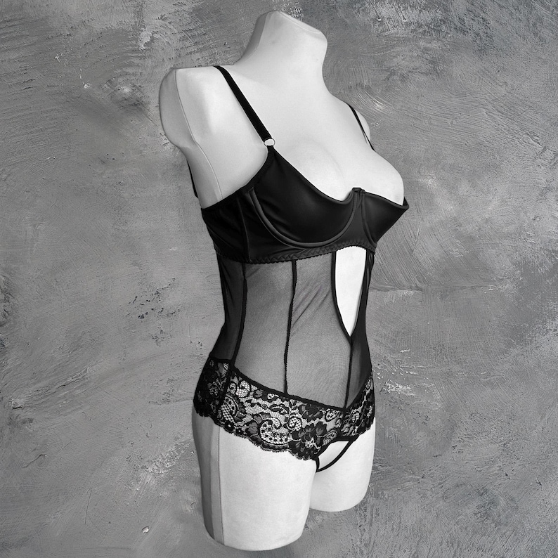 May include: Black lingerie bodysuit with a sheer mesh bodice and lace trim. The bodice has a sweetheart neckline and a cutout detail at the center.