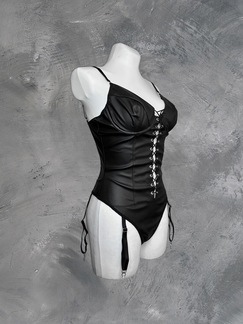 May include: A black leather corset with a lace-up front and adjustable straps. The corset has a garter belt with straps attached.