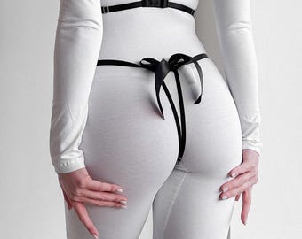 Op de afbeelding: Witte body met een zwart verstelbaar riemtuig en een zwarte strik aan de achterkant.