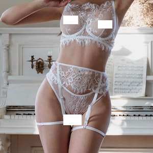 Op de afbeelding: Witte kanten lingerie set met een beha, een slip met hoge taille en een jarretelgordel. Het delicate bloemenkanten ontwerp bedekt de bh-cups en de slip. De set is gemaakt van een transparante, lichtgewicht stof.