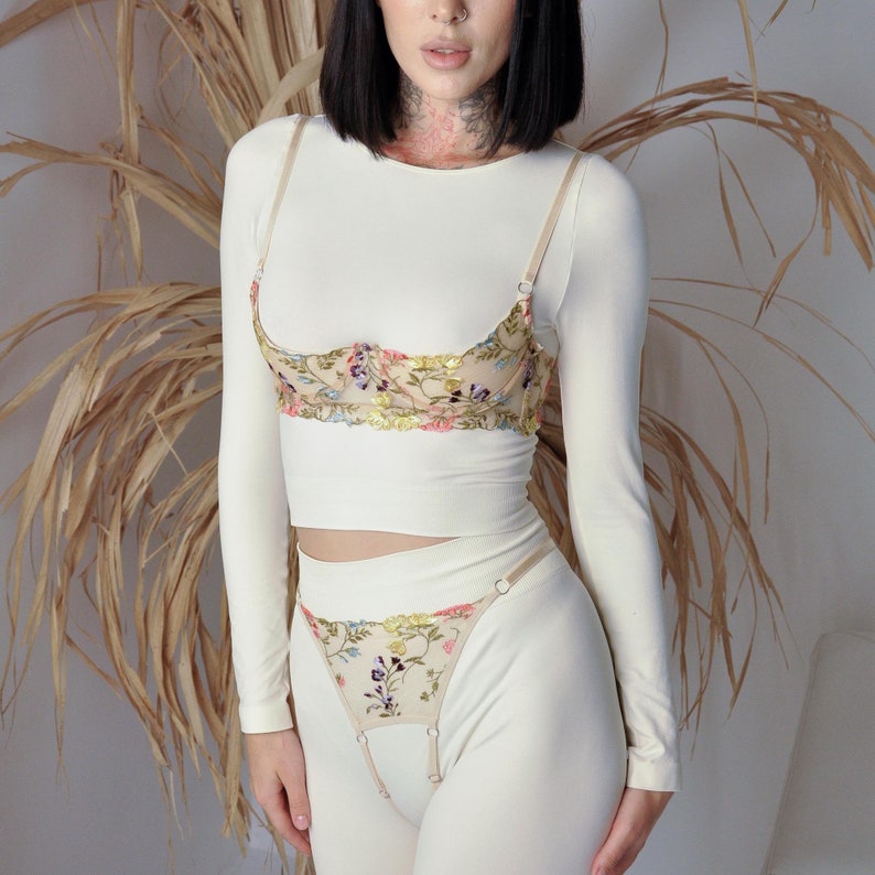 May include: A white long-sleeved top with a floral embroidered bra and matching panty set. The bra has adjustable straps and a delicate floral design. The panty has a high waist and a matching floral design.