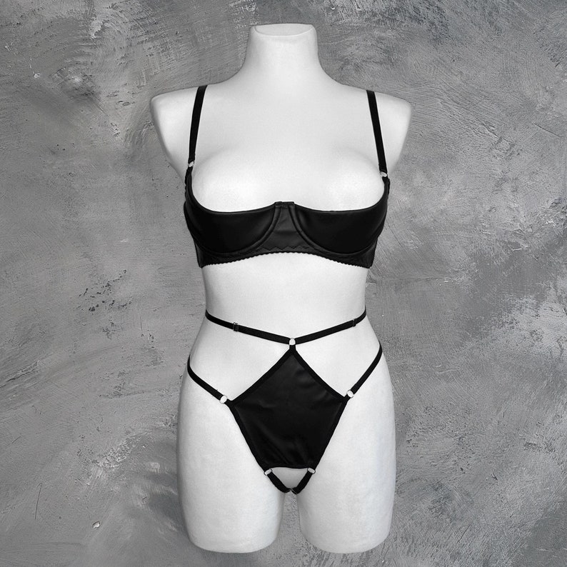 May include: Black lingerie set with a satin bra and matching panty. The bra has a plunging neckline and the panty has a criss-cross strap design.