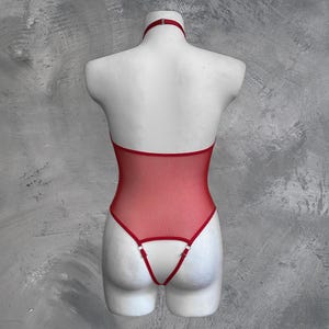 May include: Red mesh bodysuit with a halter neck and adjustable straps. The bodysuit has a low back and a thong style bottom.