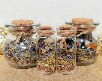May include: Four glass jars with cork lids filled with dried herbs, crystals, and other natural elements. The jars are arranged in a row on a brown surface with a patterned design.