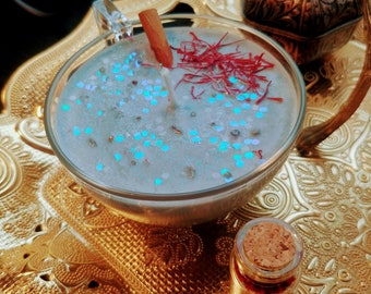 Peut inclure: Une bougie bleu turquoise avec des paillettes et un bâton de cannelle dans une tasse à thé en verre. La bougie est sur un plateau doré avec une petite bouteille en verre avec un bouchon en liège.