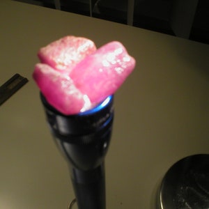 Op de afbeelding: Drie roze edelstenen worden in een zaklamp gehouden. De edelstenen zijn doorschijnend en hebben een lichte glans.