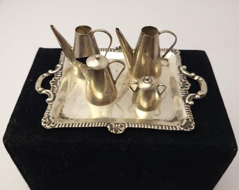 May include: A silver tea set with a teapot, creamer, and sugar bowl on a silver tray. The set is miniature in size and appears to be made for dollhouse use.