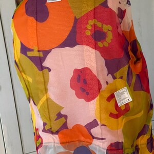 May include: A sheer, floral-print top with a vibrant mix of colors including orange, pink, yellow, and purple. The top features a large floral pattern and a tag that reads "CHANEL". The garment is lightweight and appears to be made of a delicate fabric.