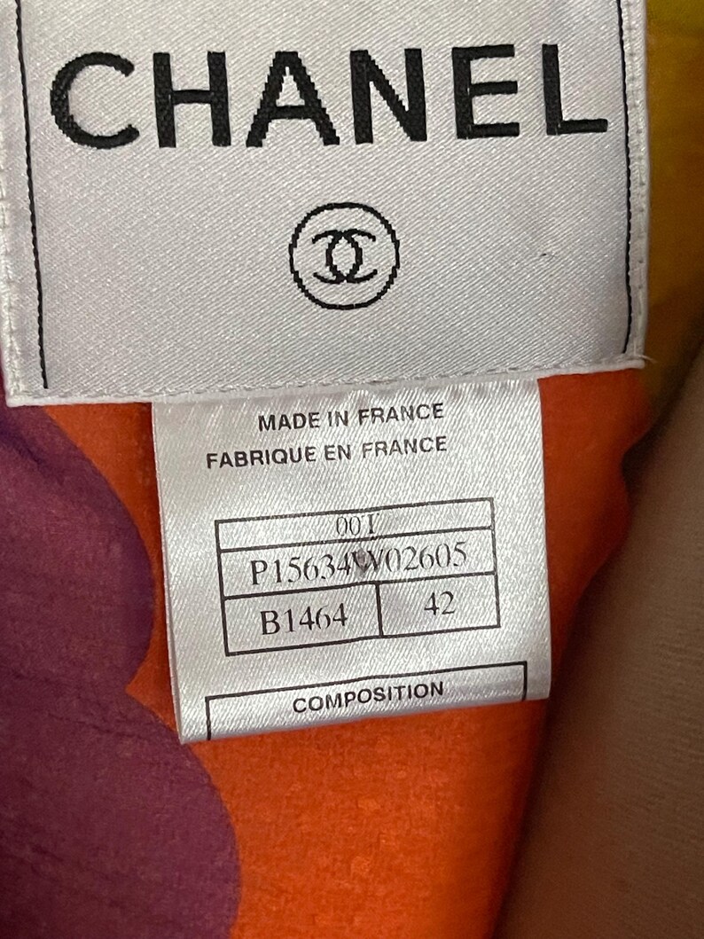 May include: Close-up of a label with the word "CHANEL" in black capital letters. Below the text is the Chanel logo, a pair of interlocking Cs. The label also includes text that reads "MADE IN FRANCE" and other product information.