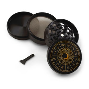 May include: Black metal grinder with a gold zodiac design. The grinder has a circular design with the zodiac symbols and a crescent moon in the center. The grinder is made of four parts: a lid, a top chamber, a bottom chamber, and a catch tray.