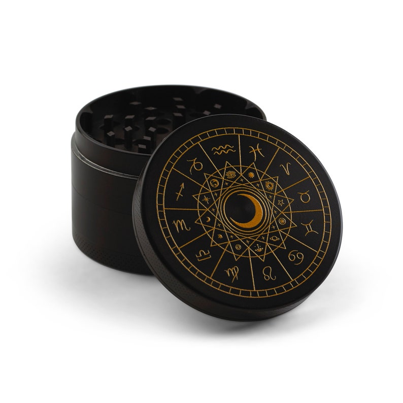 May include: Black metal grinder with a gold zodiac wheel design featuring a crescent moon and all 12 zodiac signs.