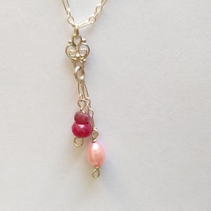 May include: A silver chain necklace with a delicate pendant featuring a cluster of red and pink gemstones.