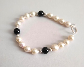May include: A bracelet featuring a series of off-white, irregularly shaped freshwater pearls interspersed with three smooth, round black beads and small, ribbed silver-toned metal spacers, finished with a silver-toned toggle clasp closure.