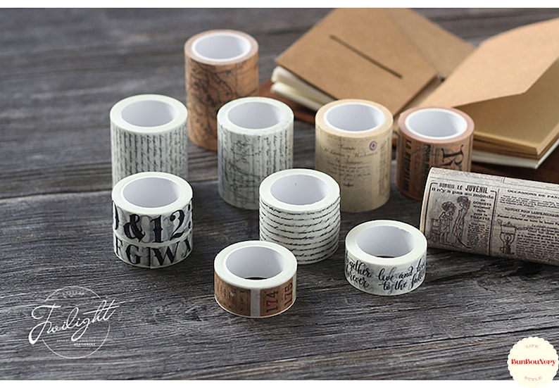 May include: Assortment of eight decorative washi tapes with various patterns, including numbers, script, and vintage illustrations. The tapes are rolled and displayed on a wooden surface.