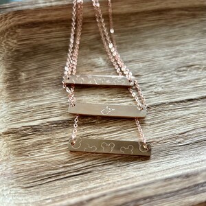 May include: Three gold bar necklaces with different designs. The top bar has a star and a Mickey Mouse head design. The middle bar has a state of Tennessee design. The bottom bar has three Mickey Mouse heads.