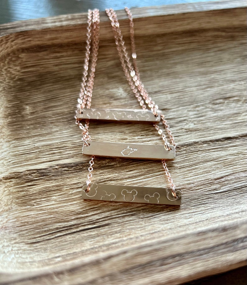 May include: Three gold bar necklaces with different designs. The top bar has a star and a Mickey Mouse head design. The middle bar has a state of Tennessee design. The bottom bar has three Mickey Mouse heads.