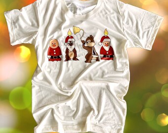 Può includere: Maglietta bianca con una grafica di quattro scoiattoli vestiti da Babbo Natale. Gli scoiattoli tengono candele e un campanello. Il testo "Chipmunk Christmas" è stampato sotto la grafica. Il testo "Elaine & Joy Co." è stampato nella parte superiore della maglietta.