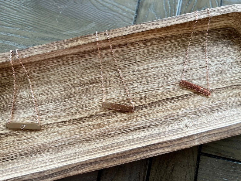 May include: Three gold necklaces with a bar pendant. Each bar pendant has a different design.