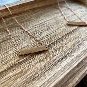 May include: Two gold necklaces with a bar pendant featuring a Mickey Mouse silhouette and stars. The necklaces are on a wooden surface.