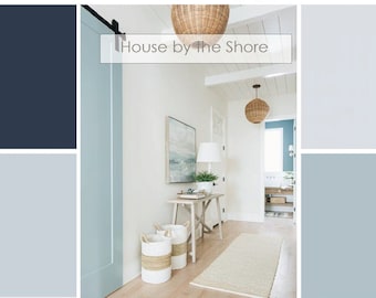 May include: A white hallway with a light blue door and a white table with two woven baskets. The hallway has a white ceiling with exposed beams and a white rug on the floor. The text "House by the Shore" is written in black on a white background.