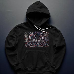 Może przedstawiać: Czarna bluza z kapturem z nadrukiem przedstawiającym szarżującego bizona, kask do futbolu amerykańskiego i nieśmiertelniki. Tekst głosi Buffalo Bills, Go Bills oraz Discipline Builds Champions. Projekt zawiera czerwone, białe i niebieskie akcenty.