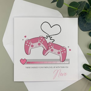 May include: A pink and white card with a pink video game controller and a heart. The card says "There's nobody I'd rather level up with than you" and "Neve".