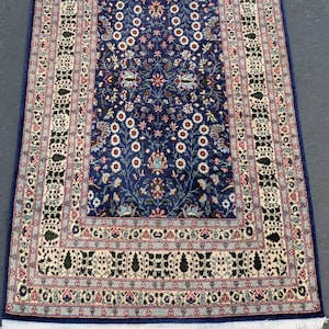 May include: A rectangular, navy blue rug with an intricate floral pattern. The rug features a central design of stylized flowers and leaves in white, pink, and blue. The border is cream-colored with a repeating geometric pattern. The rug is approximately 8 feet long.