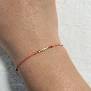 May include: A red string bracelet with a gold charm that says "Infinito".