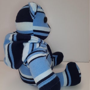 May include: A blue and navy striped plush teddy bear wearing a matching hooded sweatshirt. The bear is sitting with its legs crossed and has black button eyes.