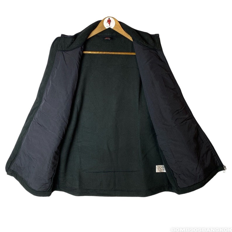 May include: A black fleece jacket with a zip fastening and a black lining. The jacket has a stand-up collar and two pockets on the front.