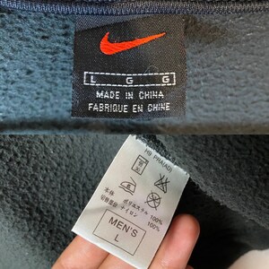 May include: Black Nike sweatshirt with a white tag that says "Made in China" and "Fabrique en Chine". The tag also has a size L and a Nike swoosh logo. The sweatshirt has a white tag with washing instructions and a size L.