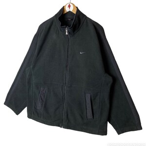 May include: Black fleece zip-up jacket with a Nike logo on the left chest. The jacket has a high collar and two pockets.