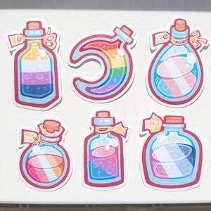 Puede incluir: Seis pegatinas coloridas que representan botellas de vidrio con tapones de corcho y líquido de color arcoíris. Las botellas tienen etiquetas con texto escrito a mano. Una pegatina representa una luna creciente con líquido de color arcoíris.