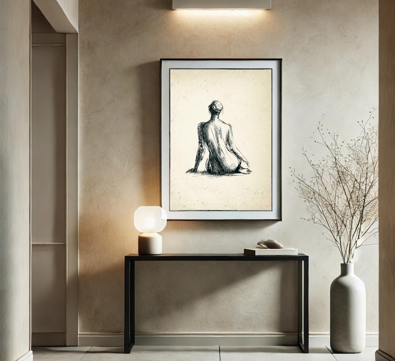 May include: A black and white line drawing of a person sitting with their back to the viewer, framed in a black frame and hanging on a beige wall.