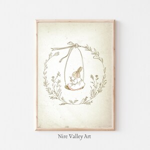 May include: A brown bunny wearing a white dress with pink trim sits on a swing made of twine and surrounded by a wreath of green leaves and white flowers. The image has a vintage aesthetic and is titled "Nire Valley Art".