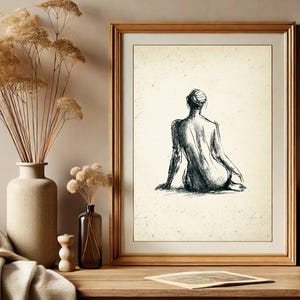 May include: A black and white line drawing of a person sitting with their back to the viewer. The drawing is framed in a light wood frame and is hanging on a wall.